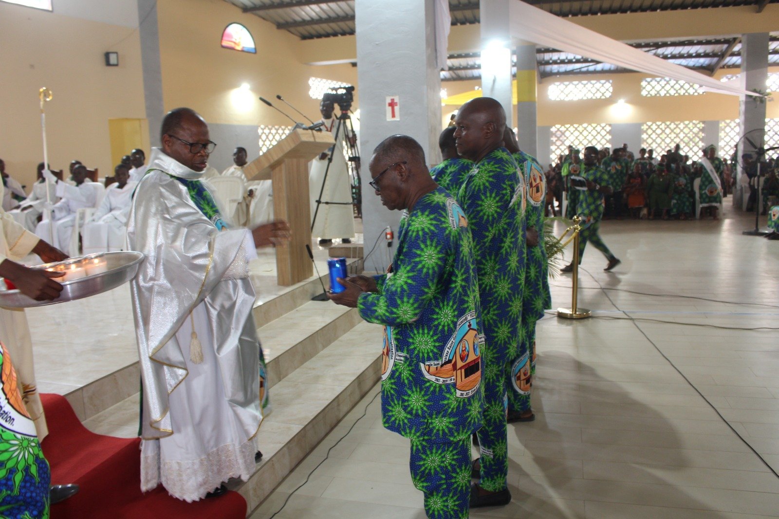 Le Père Damien Ogué remettant 12 cierges allumés à 12 fidèles à poser sur les 12 piliers oints avec le Saint Chrême